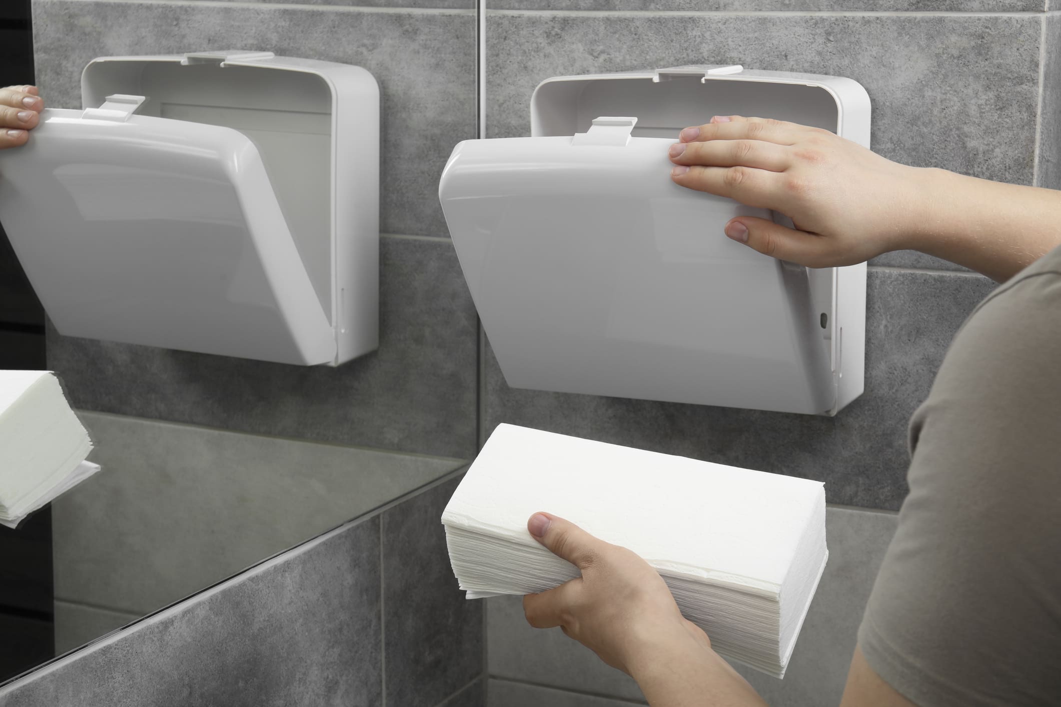 Woman putting new fresh paper towels into dispenser in bathroom