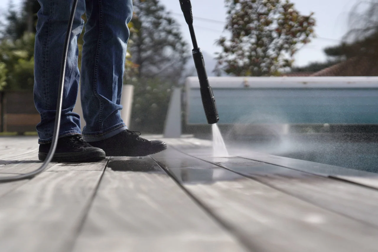 Man wearing jeans using a high pressure cleaner to clean a wooden deck
