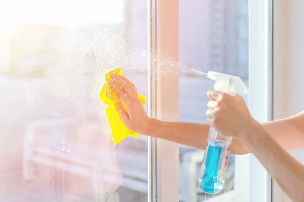 Woman spraying window cleaner on a window and wiping with a yellow cloth