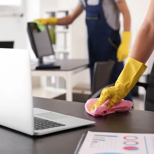 Woman wearing yellow gloves cleaning an office desk with a pink cloth